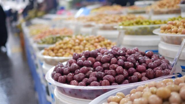 A vibrant assortment of pickled olives and other food items displayed on an outdoor market stall, offering a close-up view of the variety of colors and textures available