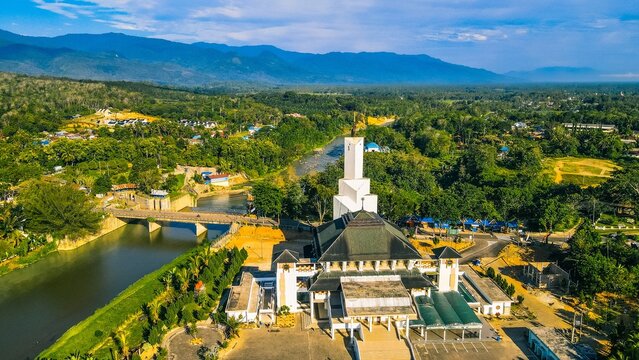Panyabungan, North Sumatra, Indonesia - 23 March 2022: Aerial view of Masjid Agung Nur Ala Nur mosque featuring its prominent tower and dome, situated near a river and bridge amidst lush greenery.