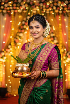 young indian woman wearing traditional sari holding pooja thali standing at home