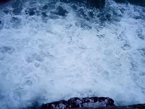 Close overhead footage of vigorously agitated seawater covered in dense white foam, with turbulent currents creating layered textures and constantly changing patterns across the surface.