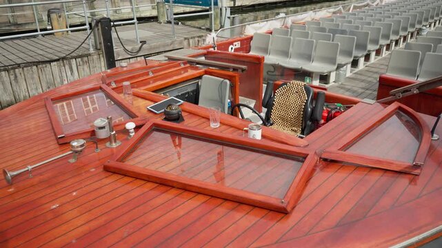 A wooden canal tour boat rests at a Copenhagen dock. Rows of passenger seats fill the deck behind the steering wheel. The classic vessel awaits guests for a scenic summer harbor excursion.