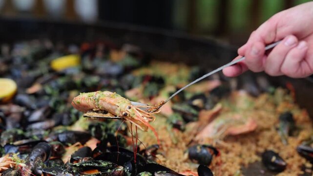 Chef cooking large pan of seafood paella with mussels, shrimp and lemon. Street food preparation at market. Traditional spanish rice dish with shellfish