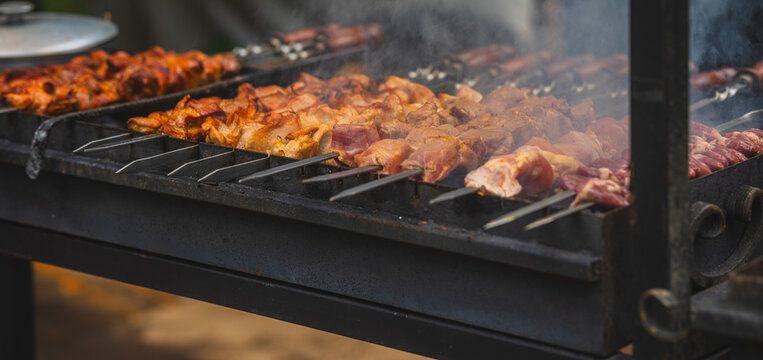 Meat skewers grilling on barbecue with smoke rising. Shashlik roasting over charcoal grill. Street food cooking, picnic and outdoor barbecue concept.