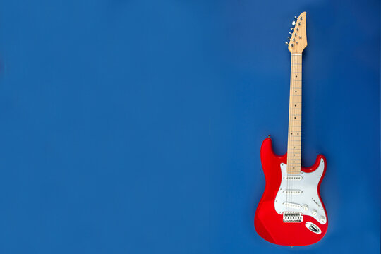 Red electric guitar on blue background. Classic solid body string instrument with maple neck and white pickguard, modern music concept with copy space.