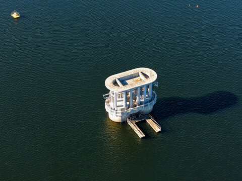 Silvan, Australia - 01 September 2026: Aerial view of the Silvan Reservoir intake tower, a concrete structure rising from the deep water, casting a long shadow on the surface.