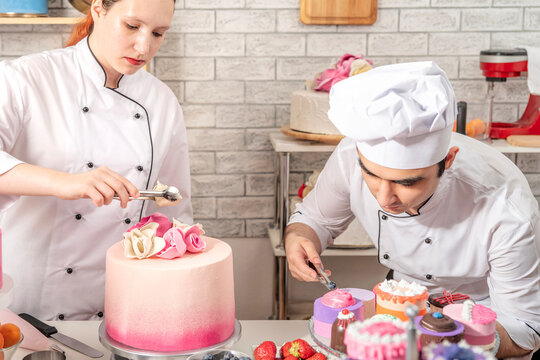Confectioners working together on detailed dessert preparation at a worktable in a small artisan bakery kitchen