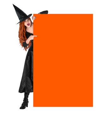 Halloween Witch, red-haired woman in witch costume and hat pointing to empty board for copy space. Halloween concept, spooky holiday mockup for text or advertising design.
