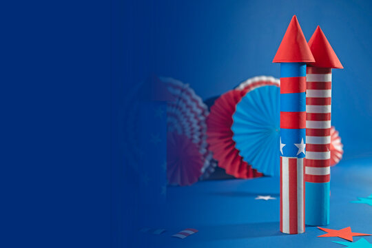 Fourth of July USA Independence Day festive celebration concept with copy space. Handmade craft paper rockets decorated with stars and stripes, USA flag, fans, blue background