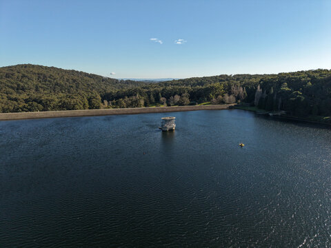 Silvan, Victoria, Australia - 01 September 2026: Aerial view of Silvan Reservoir Park with its central valve tower, surrounded by dense forest and calm water under a clear blue sky.