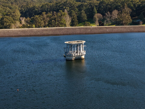 Silvan, Australia - 01 September 2026: Aerial view of the Silvan Reservoir Park valve tower rising from deep blue water, surrounded by dense forest and a stone embankment.