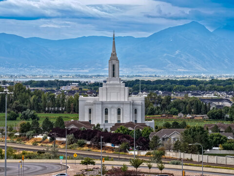 Orem, Utah, United States - 30 August 2026: Aerial view of Orem Utah Temple with surrounding residential neighborhoods, green fields, and the Wasatch Range under a cloudy sky.