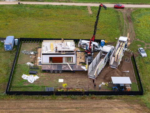 Gdansk, Poland - 31 August 2026: Aerial view of modular house construction with a crane and transport trucks on site.