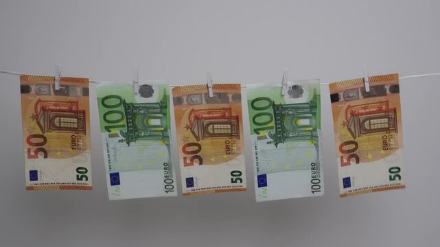 Five euro banknotes of fifty and one hundred denominations hang on a white rope, showing money laundering concept.