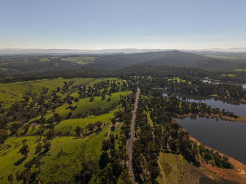 Christmas Hills, Victoria, Australia - 31 August 2026: Aerial view of Sugarloaf Reservoir with rolling green hills, eucalyptus trees, and a winding road under a clear sky.