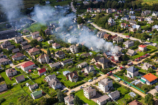 Kaunas, Lithuania - 27 August 2026: Aerial view of a residential neighborhood with a house on fire, surrounded by emergency vehicles and smoke rising into the air.