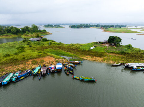 Rangamati, Bangladesh - 31 May 2025: Aerial view of traditional wooden boats docked along the lush green shores of Kaptai Lake under a cloudy sky.