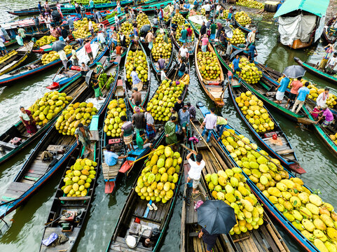 Rangamati, Bangladesh - 31 May 2025: Aerial view of a bustling floating market in Rangamati, featuring wooden boats loaded with fresh jackfruit, with traders navigating the waterway.