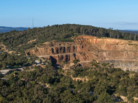 Lysterfield, Australia - 30 August 2026: Aerial view of Boral Quarries showing terraced rock faces, surrounding eucalyptus forest, and clear blue sky in Lysterfield, Victoria, Australia.