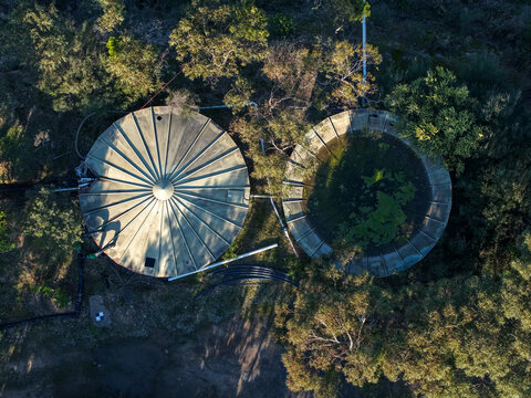 Lysterfield, Australia - 30 August 2026: Aerial view of Boral Quarries featuring two large circular water storage tanks surrounded by native eucalyptus trees and rugged terrain.