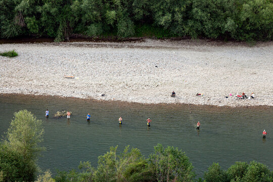 Montenegro - 26 July 2005: Aerial view of men wading in the river and fishing with rods, with a gravel bank and dense green trees along the riverbanks.