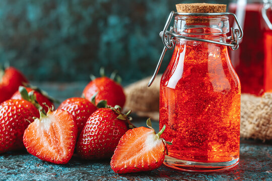 Fresh strawberries and a glass bottle filled with red berry jam on dark stone