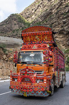 View of a vibrantly decorated truck featuring traditional Pakistani truck art, parked on a mountain road with rocky cliffs in the background in Dera Ghazi Khan, Punjab, Pakistan.