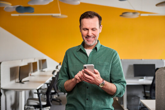 A smiling businessman uses a smartphone in a modern office