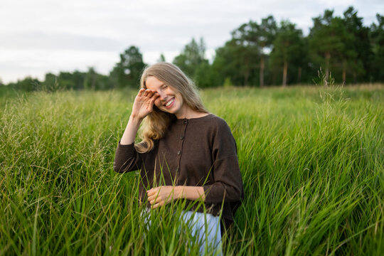 Woman smiles while standing in tall green grass during summer