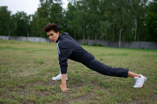Athletic woman performs a warmup stretch on a grassy field outdoors