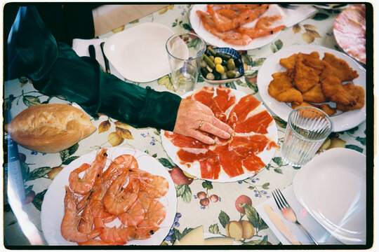 Senior woman reaches for jamon iberico at a family lunch table