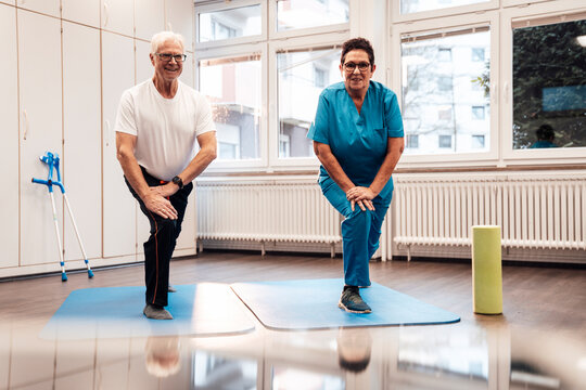 Physiotherapist guiding senior in physiotherapy exercise on mat indoors