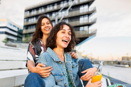 Happy female friends hug and hold a drink outdoors in Hamburg
