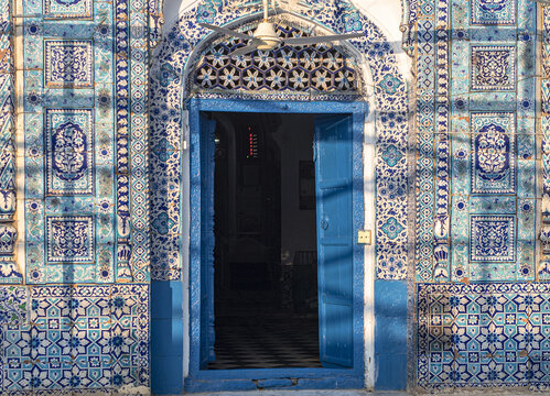 View of the intricate blue and white floral tile work surrounding the arched entrance and bright blue wooden door of the Shrine of Shah Abdul Latif Bhittai in Bhit Shah, Sindh, Pakistan.