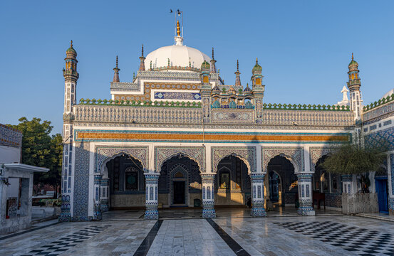 View of the Shrine of Shah Abdul Latif Bhittai with its intricate blue and white tile work, arched entrances, and white dome under a clear blue sky in Bhit Shah, Sindh, Pakistan.