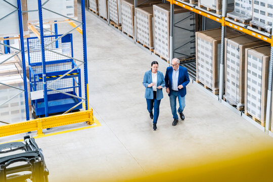 Businessman and businesswoman walk through a warehouse with a tablet