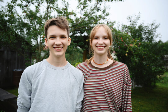 Smiling teenage boy and girl stand together in a summer garden