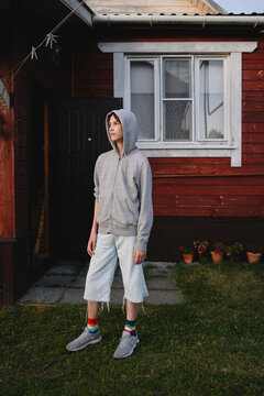 A teenage boy stands in the yard of a red wooden house