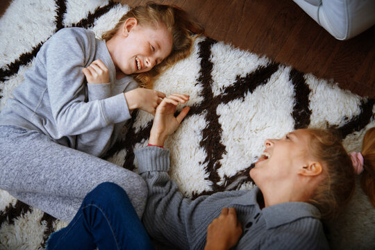 Happy sisters play and laugh on a fluffy rug indoors
