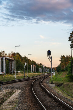 View of railway tracks with a signal light and industrial pipes running alongside a forest in Jaworzno, Silesian Voivodeship, Poland.