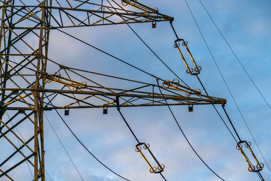 View of a high-voltage electricity pylon with metal lattice structure and power lines against a clear blue sky during golden hour in Jaworzno, Silesian Voivodeship, Poland.