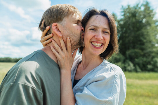 A man kisses a cheerful woman on the cheek outdoors
