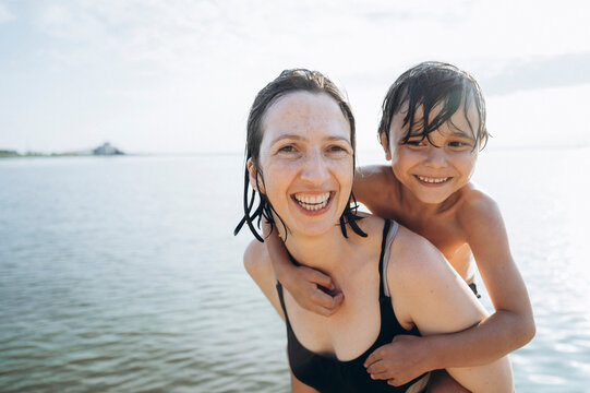 Mother and son smile while swimming together at the beach in summer