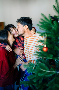 A father kisses his son while the mother smiles near a Christmas tree
