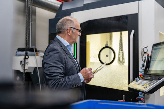 Male manager with tablet inspecting machinery in production hall
