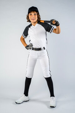 Male youth baseball player in full uniform, standing and smiling with bat over shoulder and hand on hip