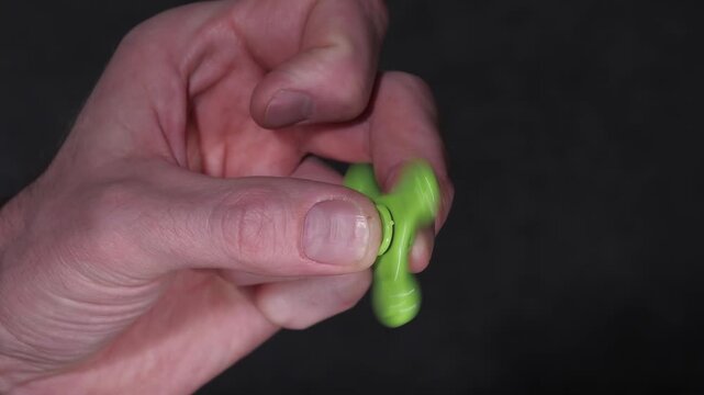 Close-up of a hand gripping a green fidget spinner, demonstrating the spinning motion in a series of frames, with a dark background emphasizing the action and focus on the spinner
