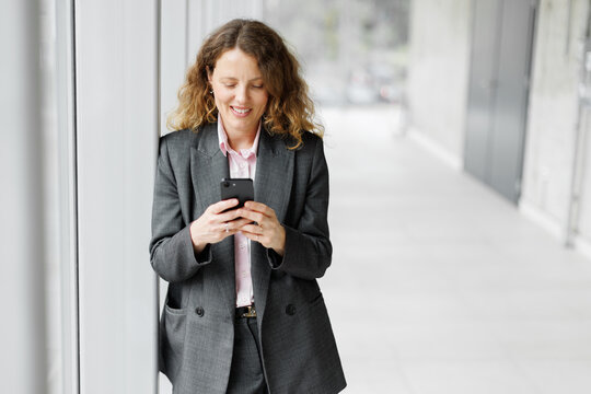 Thoughtful businesswoman uses mobile phone in the office corridor