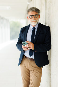 Thoughtful businessman holds a smartphone in an office corridor