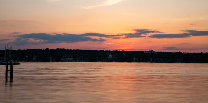 View of a calm lake at sunset with silhouettes of trees and buildings on the horizon and a wooden pier in the foreground in Berlin, Berlin, Germany.