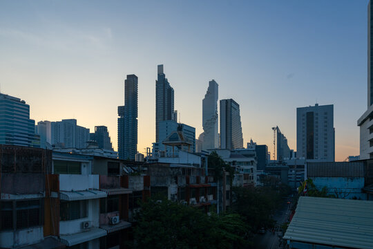 View of the modern Bangkok skyline featuring the distinctive pixelated MahaNakhon building rising above low-rise residential rooftops at dusk in Bangkok, Bangkok, Thailand.